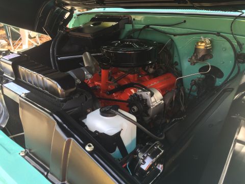 1962 Chevrolet Suburban - Close-up view of the engine bay of a classic Chevrolet Suburban, featuring a bright orange V8 engine, black air cleaner, and green painted…