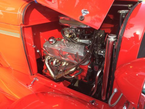 1962 Chevrolet Suburban - Close-up view of a shiny red engine bay in a classic vehicle. The engine features a chrome "COBRA POWERED BY FORD" valve cover and red spar…