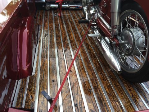 1962 Chevrolet Suburban - A vintage motorcycle is secured with a red strap in the bed of a classic pickup truck with a wooden and metal slatted floor.