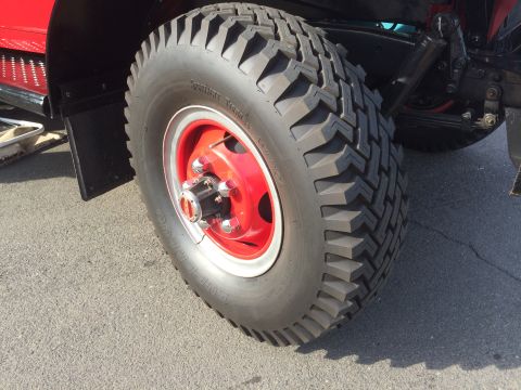 1962 Chevrolet Suburban - A close-up view of the front driver's side tire and red wheel of a vintage red vehicle. The tire has a rugged tread pattern and the wheel f…