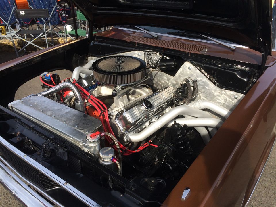 Custom V8 engine in a classic brown vehicle, featuring chrome and aluminum parts, red spark plug wires.
