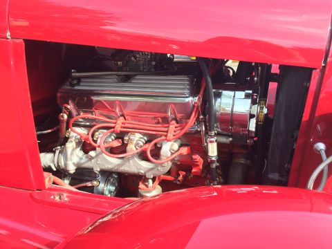 1962 Chevrolet Suburban - A close-up view of a red classic vehicle's engine bay, featuring a chrome-finished engine with red spark plug wires and exhaust manifolds.