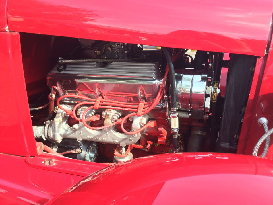 Close-up of a red classic car engine bay with chrome details and red spark plug wires.