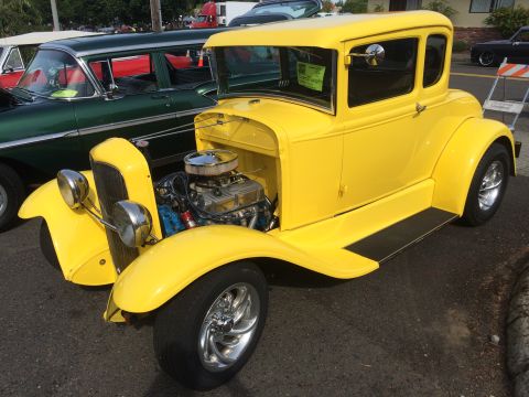 1962 Chevrolet Suburban - A bright yellow hot rod coupe is parked next to a dark green station wagon. The hot rod features an exposed engine with chrome accents and…