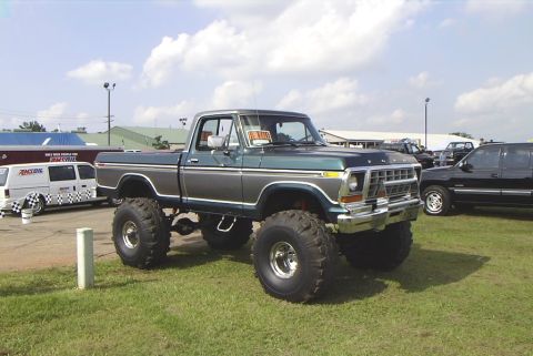 1995 Ford Bronco - This lifted pickup truck is parked on grass at an outdoor event, with other vehicles nearby.