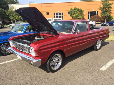 1962 Chevrolet Suburban - A shiny red 1960s era pickup truck with its hood open is parked on asphalt. The truck has chrome accents and custom wheels, and a blue pick…