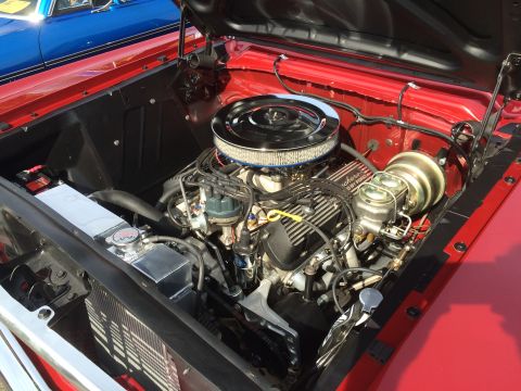 1962 Chevrolet Suburban - The open hood reveals a red vehicle's engine bay, featuring a chrome air cleaner, V8 engine, and aluminum radiator. A blue vehicle is visib…