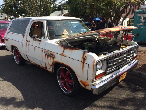 1962 Chevrolet Suburban - A two-door SUV in worn white paint with heavy rust patina, red five-spoke wheels and hood raised, displayed at a car show; a 'Rat Charger'…