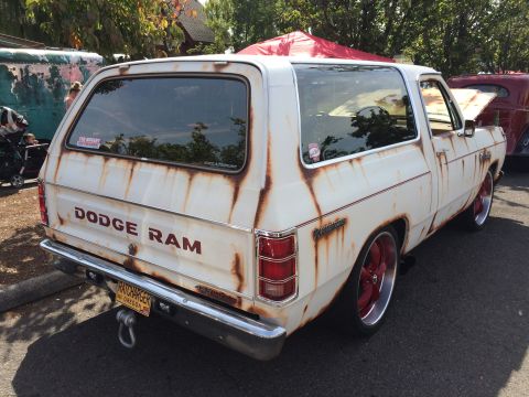 1962 Chevrolet Suburban - The rear driver's side of a heavily rusted white Dodge Ram SUV with red trim and custom red wheels. The vehicle has a "DODGE RAM" decal on…