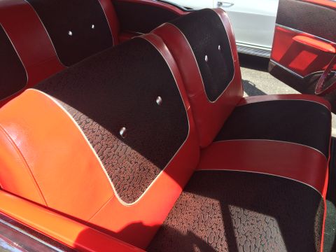 1962 Chevrolet Suburban - The interior of a classic car features red and black patterned upholstery on the seats, with red leather trim and chrome accents. Sunlight…