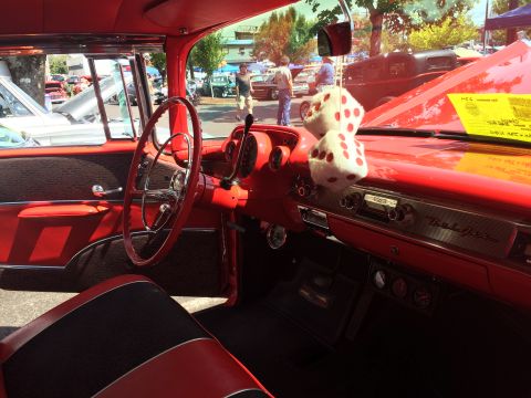 1962 Chevrolet Suburban - Interior view of a classic red Chevrolet, focusing on the dashboard and steering wheel. Fuzzy dice hang from the rearview mirror, and a yel…