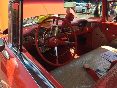 1962 Chevrolet Suburban - Interior view of a classic red Chevrolet with a tan textured seat and a red steering wheel. A fuzzy red die hangs from the rearview mirror.