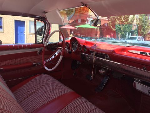 1962 Chevrolet Suburban - Interior view of a vintage red Chevrolet with a two-tone red and white steering wheel and patterned red and white seats. The dashboard is r…