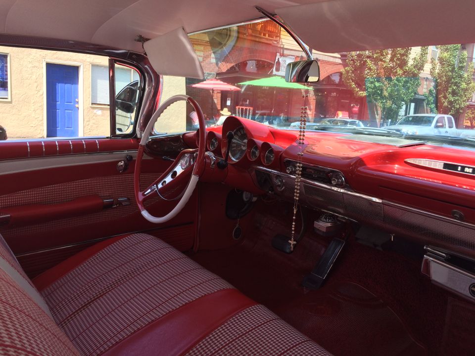Interior of a vintage red Chevrolet, showing the steering wheel, dashboard, and seats.
