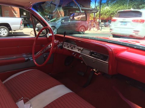 1962 Chevrolet Suburban - The interior of a classic red Chevrolet is shown, featuring a red steering wheel, dashboard with chrome accents, and striped red seats. The…