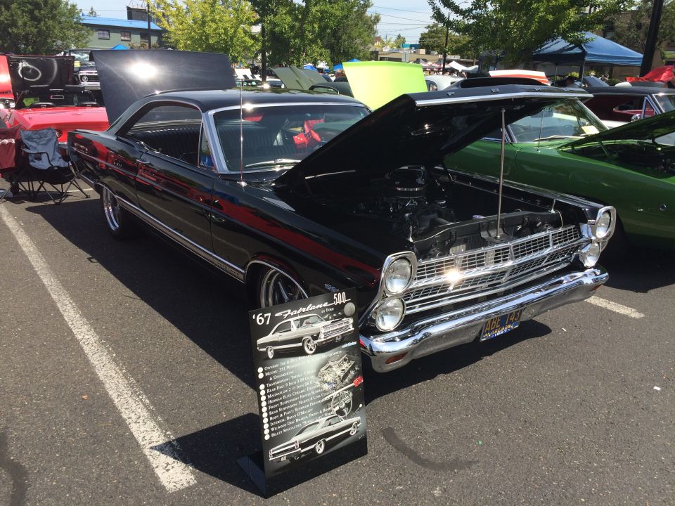 Black 1967 Ford Fairlane 500 with hood open, parked at an outdoor event.