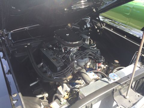 1962 Chevrolet Suburban - The open hood of a black classic vehicle reveals a detailed view of its engine bay, featuring a chrome air cleaner, black valve covers with…