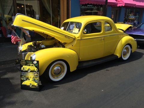 1962 Chevrolet Suburban - A bright yellow 1940 Ford Business Coupe, nicknamed "Daisy", is displayed with its hood open at an outdoor event. A sign in front of the ca…