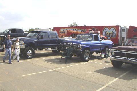 1995 Ford Bronco - A blue pickup truck with a "COUNTRY BOYS CLUB" sticker is parked next to other trucks and a trailer.