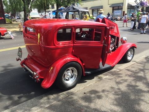 1962 Chevrolet Suburban - A bright red vintage sedan hot rod is parked on a street with its driver's side door and hood open, revealing the engine. The car has a cus…