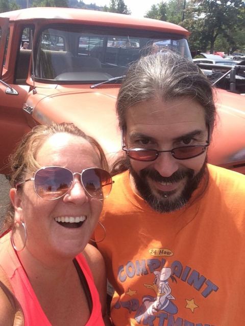 1962 Chevrolet Suburban - A woman and a man take a selfie in front of a bright orange classic Chevrolet truck. The man is wearing an orange t-shirt with a cartoon du…