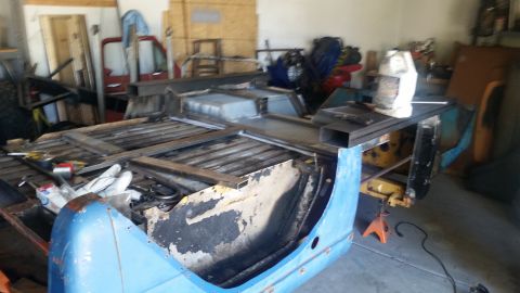 1979 Ford Bronco - A partially disassembled blue vehicle frame, likely a truck or SUV, is in a garage setting. Metal framing and various tools are laid out on…