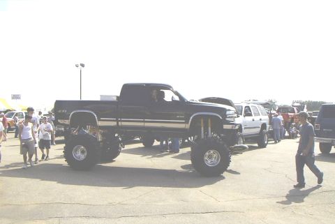 1995 Ford Bronco - Custom lifted black pickup truck on display at an outdoor event with other vehicles present.