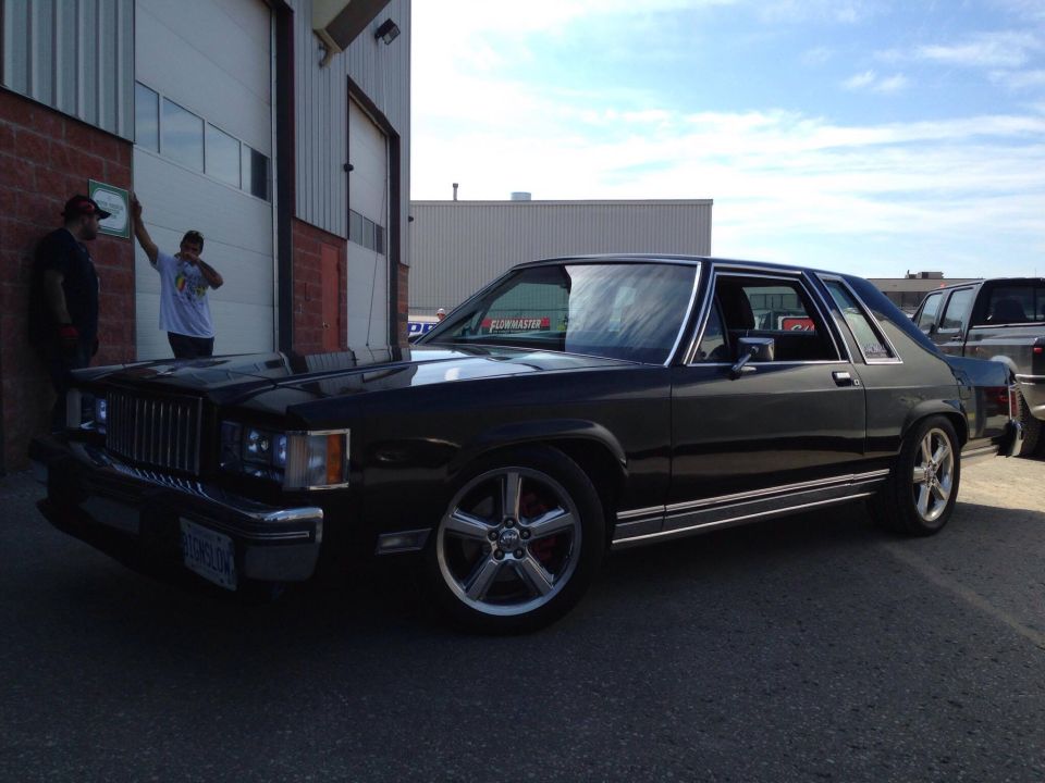 Black two-door sedan with chrome trim and aftermarket wheels parked outside a brick building.