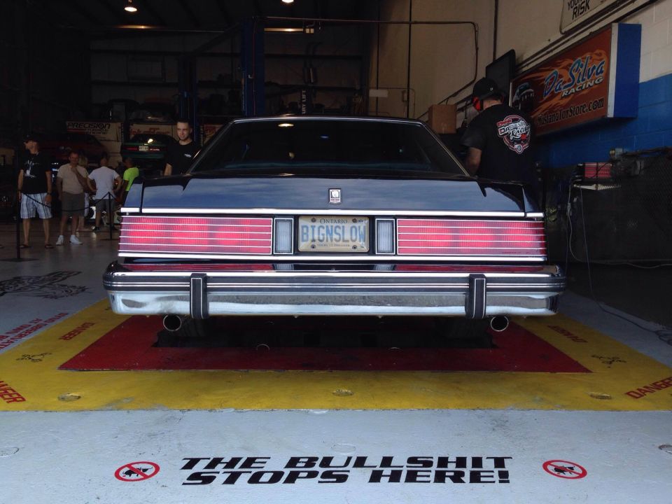 Rear view of a dark blue sedan with license plate BIGNSLOW in a garage.