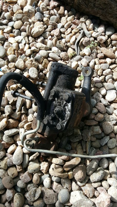 1996 Ford Bronco - A used power steering pump, covered in grime, is shown against a backdrop of small stones.