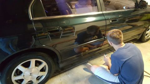 1996 Ford Bronco - Person polishing the side door of a dark sedan in a garage.