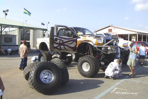 1995 Ford Bronco - A heavily modified pickup truck with custom graphics and oversized tires is parked outdoors, with people around it.