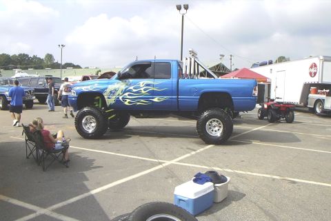 1995 Ford Bronco - A lifted blue pickup truck with custom flame graphics is parked at an outdoor event.