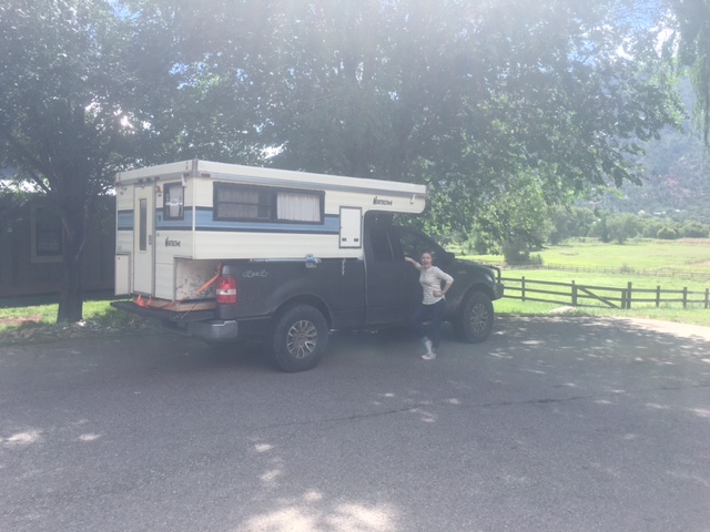 Woman posing next to a black Ford F-150 pickup truck with a camper shell.