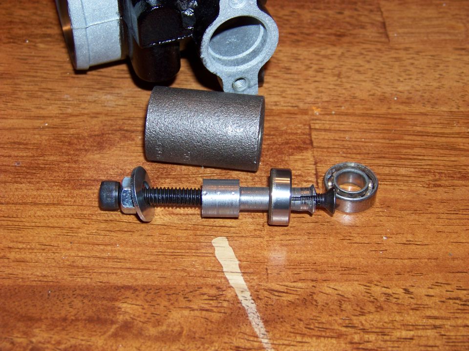 Disassembled brake caliper part with threaded rod, nut, washer, and bearing on wood.