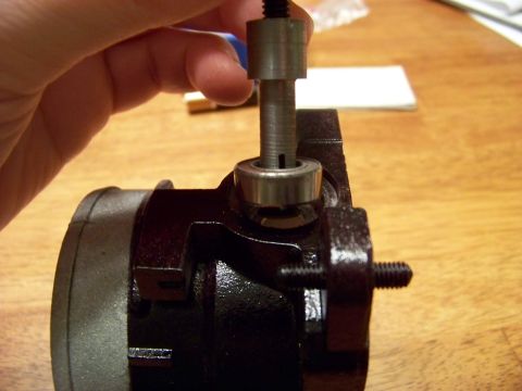 1999 Mercury Grand Marquis - A hand is holding a metal tool with a threaded rod and a bearing on the end, which is being inserted into a dark-colored mechanical compone…