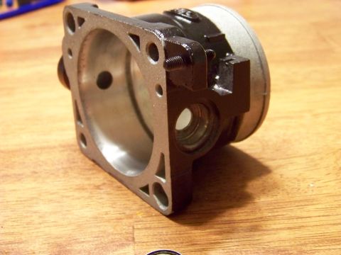 1999 Mercury Grand Marquis - A close-up, angled view of a metal automotive part, likely a throttle body or similar component, resting on a wooden surface. The part is p…