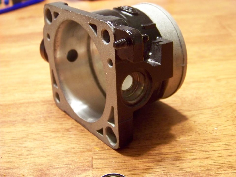 Close-up of a dark gray and silver metal automotive part on a wooden surface.