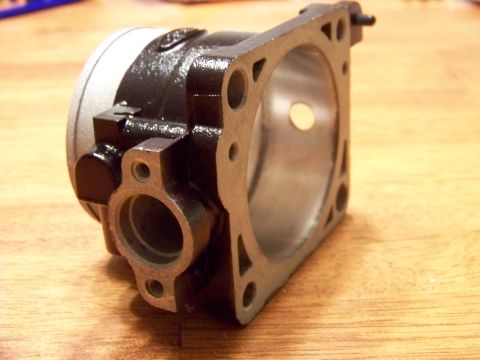 1999 Mercury Grand Marquis - A close-up, angled view of a black and silver engine part, possibly a carburetor or throttle body, resting on a wooden surface. The part fe…