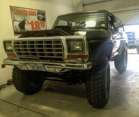 1979 Ford Bronco - A lifted, dark-colored 1979 Ford Bronco is parked inside a garage with its hood open. A sign advertising "30 PACK CANS" and "Keystone Light…