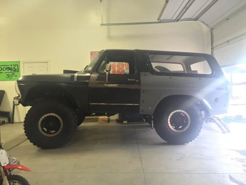 1979 Ford Bronco - A dark green Ford Bronco is parked indoors, its side profile clearly visible with large off-road tires.
