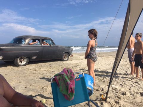 1979 Ford Bronco - A classic car sits on the beach under a blue sky with waves in the background.