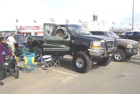 1995 Ford Bronco - A dark green Ford F-250 Super Duty truck is parked at an outdoor event with other vehicles and people around.