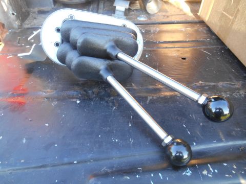 1972 Ford Bronco - A pair of shifters with black knobs and chrome shafts are shown resting on a dark surface.