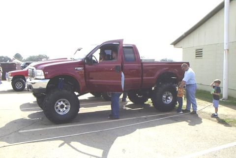 1995 Ford Bronco - A lifted maroon Ford F-250 pickup truck is displayed with people gathered around it.