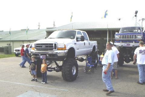 1995 Ford Bronco - A lifted white Ford pickup truck is parked next to a blue pickup truck at an outdoor event.