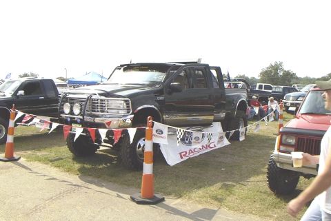 1995 Ford Bronco - A lifted black Ford F-Series truck is displayed at an outdoor event with other vehicles.