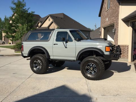 1988 Ford Bronco - This lifted Ford Bronco is parked in front of a brick house and garage on a sunny day.