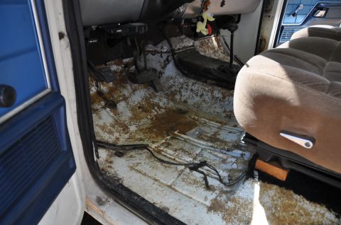 1979 Ford Bronco - The interior of a vehicle shows extensive rust and dirt on the floor, with exposed wiring.