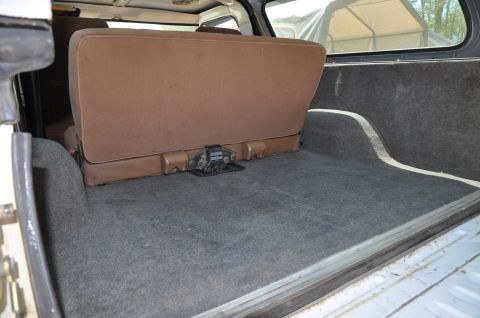 1979 Ford Bronco - The rear interior of a vehicle shows a brown bench seat and grey carpeted cargo space.